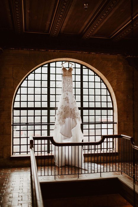 Bride's gorgeous wedding dress hanging in front of a large vintage window